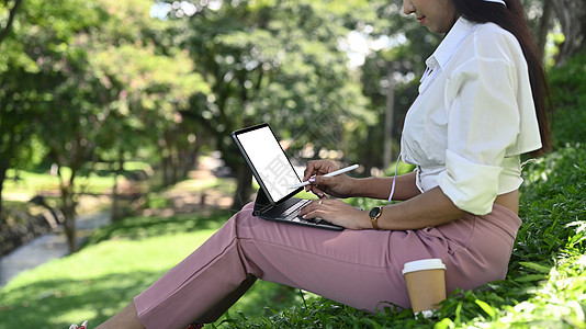 年轻女子坐在公园里 用电脑平板电脑工作图片