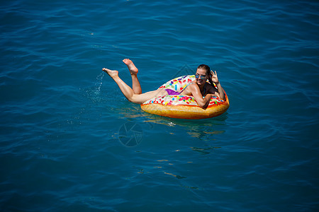 穿着泳衣的美丽快乐年轻女子 带着充气环 在蓝海中放松 阳光日光 海边度假 旅游晒黑戒指假期热带橡皮女士比基尼乐趣晴天泳装图片