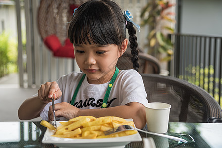 年轻的亚洲女孩吃薯条 年轻的孩子快乐的马铃薯快餐眼睛享受餐厅土豆幼儿园乐趣筹码女性女士食欲图片