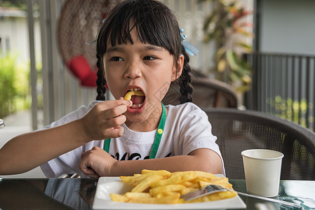 年轻的亚洲女孩吃薯条 年轻的孩子快乐的马铃薯快餐手指眼睛饥饿女儿餐厅筹码幸福幼儿园女性食欲图片