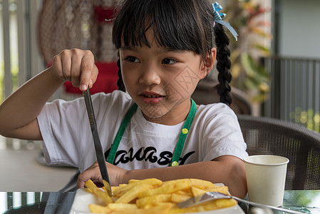 年轻的亚洲女孩吃薯条 年轻的孩子快乐的马铃薯快餐女士土豆餐厅幸福女性乐趣饥饿筹码微笑眼睛图片