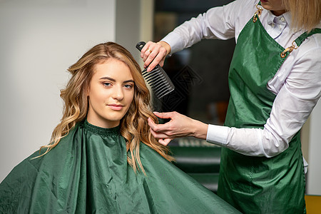 美发师一边用梳子梳头一边为女人做发型 在美发沙龙梳头治疗客户女孩金发女士理发师职业工作梳妆台头发图片