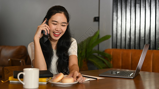 年轻漂亮的女士坐在她家办公室时 与朋友在电话上交谈愉快的年轻女孩 )图片