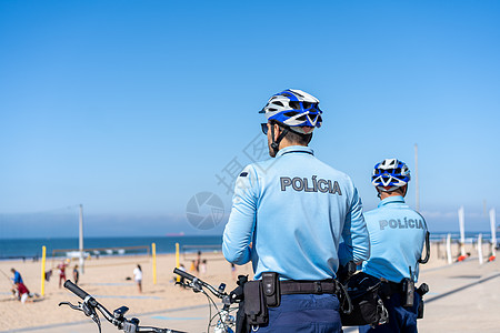 两名警察骑着自行车巡逻海边列车 人们在大西洋海岸的城市公共海滩晒太阳 美国海军陆战队警官旅游头盔安全天空街道长廊民众海洋热带图片