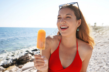 可爱的年轻姑娘夏天在海滩吃橘子冰棒图片