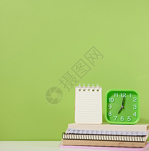一张开着的纸条和绿闹钟 站在一堆笔记本上 一个绿色的背景图片