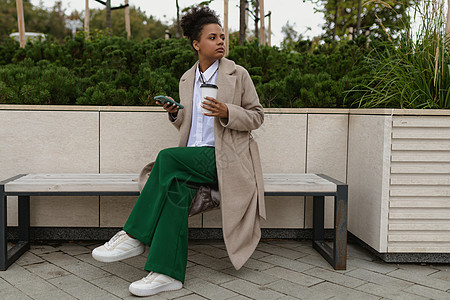 一名非裔美国妇女坐在公园的长椅上 手持笔记本电脑 手机在距离很远处看似十分周密图片