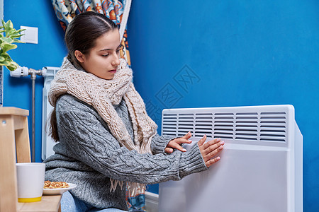 穿着毛衣围巾的少女在电暖气散热器附近升温图片