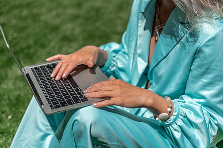 一位美丽的年轻女子 金发卷发戴眼镜 穿着蓝裙子 在大自然的草地上坐着 用笔记本电脑技术药片金发女郎房子自由职业者女性微笑稻草公寓图片