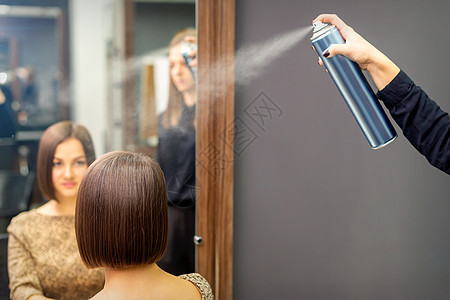 理发师用喷发剂修补坐在理发厅的年轻黑发女郎的短发型化妆品外貌发型师女性造型师喷涂女士治疗男人香味图片