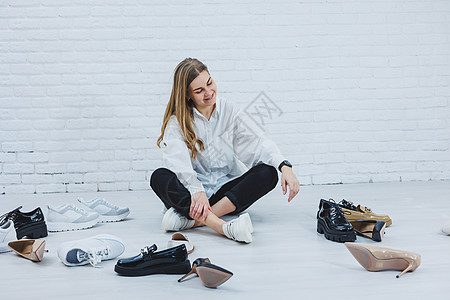 一位年轻女子坐在地板上的鞋子中间 为自己挑选新鞋 穿白衬衫和黑裤子的女士 穿白鞋的女人鞋类办公室女孩内阁商业运动购物店铺成人零售图片