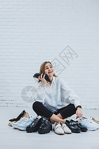 身着白色衬衫和黑色裤子的时髦服装 微笑着的快乐美丽的年轻女人坐在鞋子中间的地板上 为自己选择一双新鞋技术地面派对运动鞋女孩衣服店图片