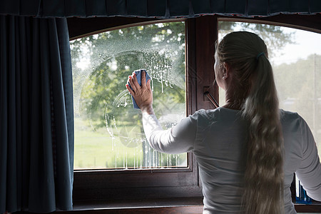 妇女用特殊的玻璃清洁器打扫窗户 通过肥皂般的窗户看房子化学品阳光清洁工泡沫橡皮灰尘女孩窗格工作图片
