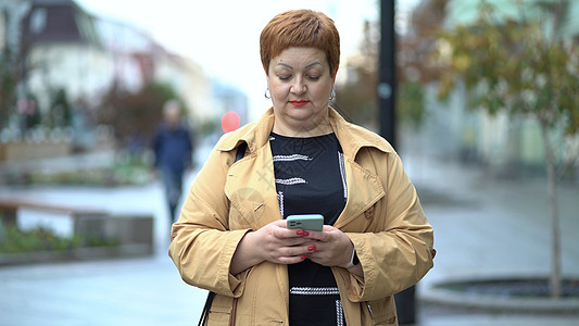 穿着秋衣的中年妇女站着 在网上聊天 在互联网上闲聊时 她们可以使用手机图片