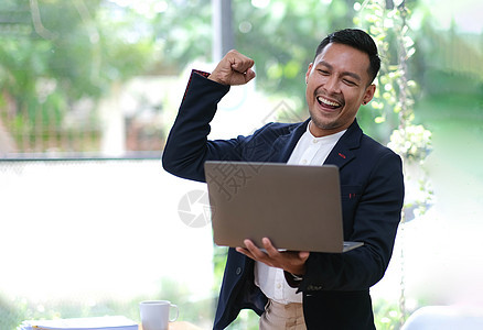 亚洲商务人士欢乐地喊叫 举起手来 庆祝胜利 男子在办公室工作 看笔记本电脑屏幕图片
