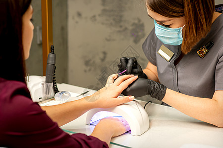 专业美甲 一位美甲师正在一家美容院用紫色指甲油为客户的女性指甲上色 特写 美容行业概念美容师奢华抛光手指女士光泽度紫外线搪瓷沙龙图片