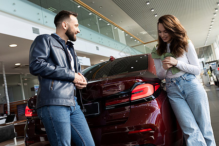 快乐的年轻夫妇 在汽车经销商中选择一辆新车 微笑地彼此交谈图片