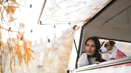 白种女人向车窗外看 拥抱她的狗杰克罗素泰瑞尔 在秋天搭露营车皮快乐动物旅行感情宠物微笑卡车露营者女孩图片