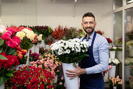 冰箱里鲜花盛开的男花商手里拿着一个花瓶 手里拿着活植物 微笑着看着镜头图片