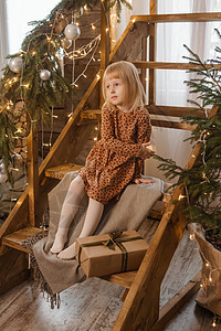一个金发女孩坐在一个 斯堪的纳维亚内部装饰的木制楼梯上裙子彩灯幸福客厅孩子婴儿圣诞家居拥抱脚步图片