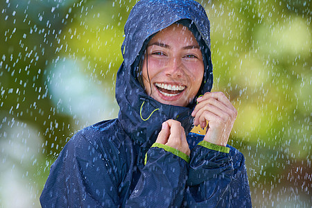 一个年轻女子带着雨衣在雨中快乐地站着 她的雨衣也很好图片