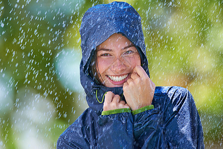一个年轻女子带着雨衣 快乐地站在雨中 穿着雨衣 (笑声)图片