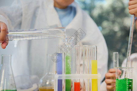 在化学课上 专注于将量筒中的水倒入装有彩色化学液体的试管中图片