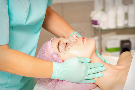 戴着手套的美容师在女性脸上涂上带去角质霜的保湿面膜 面部美容治疗 面部护理程序身体沙龙奶油电解女士温泉皮肤奢华卫生诊所图片
