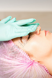 戴着手套的美容师在女性脸上涂上带去角质霜的保湿面膜 面部美容治疗 面部护理程序皮肤女士洗剂滋润温泉诊所化妆品水分保健面具图片