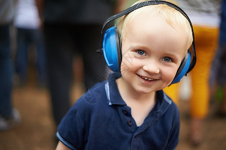 在户外节日 一个年轻男孩戴着扬声吊销耳机的近距离镜头被拍下来了乐趣微笑男生享受噪音金发女郎孩子们快乐男性童年图片