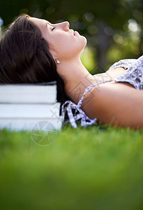 让你的思绪漫游一位年轻女子躺在公园里 头靠在一堆书上教育大学学生学者草地花园冷藏读者图书青年图片