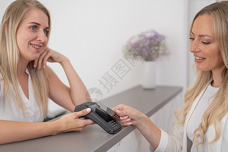 年轻女性在美容院用信用卡支付费用 使用NFC的无接触付款电子商务互联网银行业柜台沙龙交易信用客户出纳员近场图片