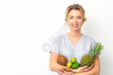 一位年轻caucasian笑着的女性营养学家的肖像 她手上拿着不同的水果 带着白色背景专家重量女士医生平衡食物福利外套快乐药品图片