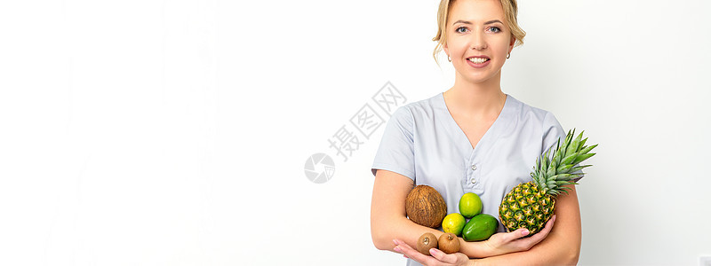 一位年轻caucasian笑着的女性营养学家的肖像 她手上拿着不同的水果 带着白色背景食物外套横幅重量营养学养分卫生专家女士顾问图片