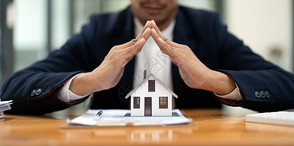 房地产概念 商务人士持有保护房屋模型 财产保险和安全概念 保护人的姿态和房子的象征图片