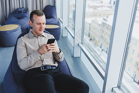 成功的男性商务人士坐在现代工作区里 查看手机上的通知 他穿着衬衫和裤子 远程工作营销咖啡企业家互联网生意设计师创造力男人员工职业图片