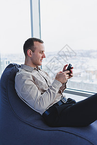 成功的男性商务人士坐在现代工作区里 查看手机上的通知 他穿着衬衫和裤子 远程工作工具设计师笔记本管理人员男人平面技术咖啡人士企业图片