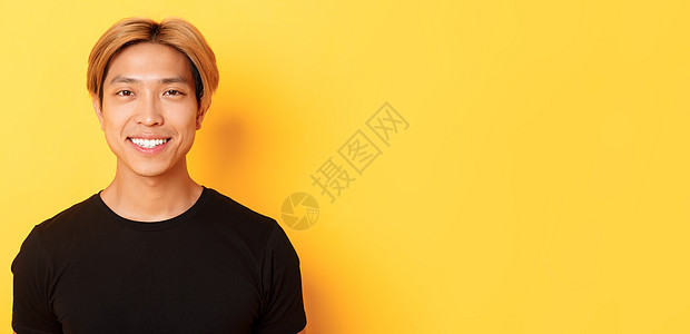 身穿黑色 T 恤的金发亚洲帅哥的特写 对着镜头笑得很开心 站在黄色背景上广告学生潮人头发理发工作室男朋友员工购物发型图片