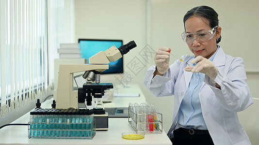 中年女研究员在研究实验室进行试管和显微镜载玻片实验图片