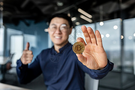 商务人士手拿着加密货币比特币的特写照片 有选择的焦点男人微笑着高兴地竖起大拇指 在现代办公楼里工作 成功的投资者图片