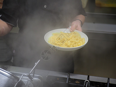 在一家餐馆专业厨房锅炉中烹饪厨师意大利面食物面条机器营养炊具收据男性平底锅火炉美食图片