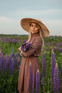 穿草帽的美女在田里走着紫色花朵 自然而然地在露天田中散步草地帽子裙子金发女郎压痛紫丁香喜悦女士稻草场地图片