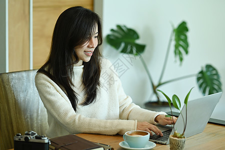 穿着白毛衣的亚洲女人 在家里用笔记本电脑图片