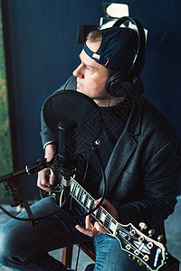 一个男歌手坐在一个椅子上 耳机里坐着一小凳子 吉他在家庭工作室录音演讲流行音乐歌曲音乐家人声居住扬声器独创性抗震电缆背景图片