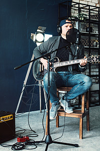 一个男歌手坐在一个椅子上 耳机里坐着一小凳子 吉他在家庭工作室录音扬声器居住嗓音流行音乐唱歌演员男性人声记录麦克风图片