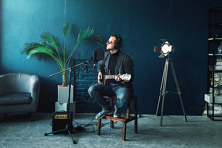 男歌手坐在凳子上 戴着耳机 吉他在家庭录音室录制曲目记录人声唱歌创新生产麦克风收音机歌曲广播唯一性图片