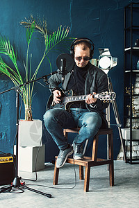 一个男歌手坐在一个椅子上 耳机里坐着一小凳子 吉他在家庭工作室录音居住嗓音演讲扬声器幸福流行音乐卡拉ok电缆演员记录图片