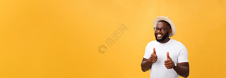 喜悦的非洲青年男子站在黄色背景上 举起拇指反脸 看摄影机时幸福男生成人经理爆炸手势微笑工作室工作快乐图片