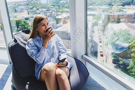 戴着耳机的年轻女经理坐在现代的合作空间里打电话喝咖啡 远程在线工作的自由职业女孩办公室员工商务音乐人士电脑企业家手机快乐电话图片