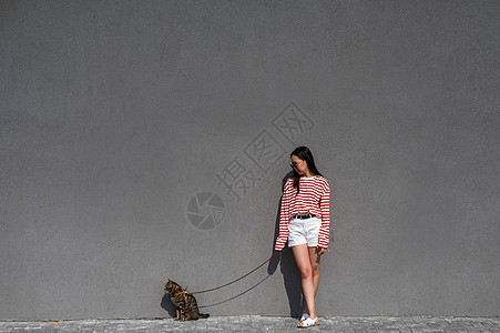 一位年轻女子带着一只灰色的小猫走在一条皮带上叶子爪子胡须捕食者宠物虎斑尾巴哺乳动物流浪汉探险家图片